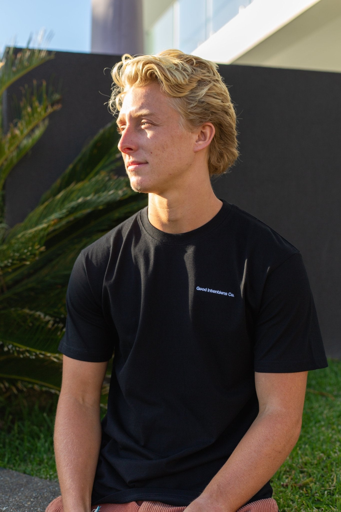 Man sitting on a wall wearing black t-shirt with white embroidered design on it 