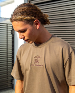 Man posing in a walnut coloured t-shirt, tshirt has a brown embroidered design 