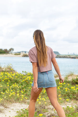 back view of woman walking through a field in hazy pink crop top